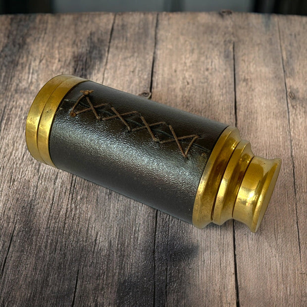 Magis Art Shop vintage-style brass monocular telescope with a dark brown stitched leather grip on a wooden surface