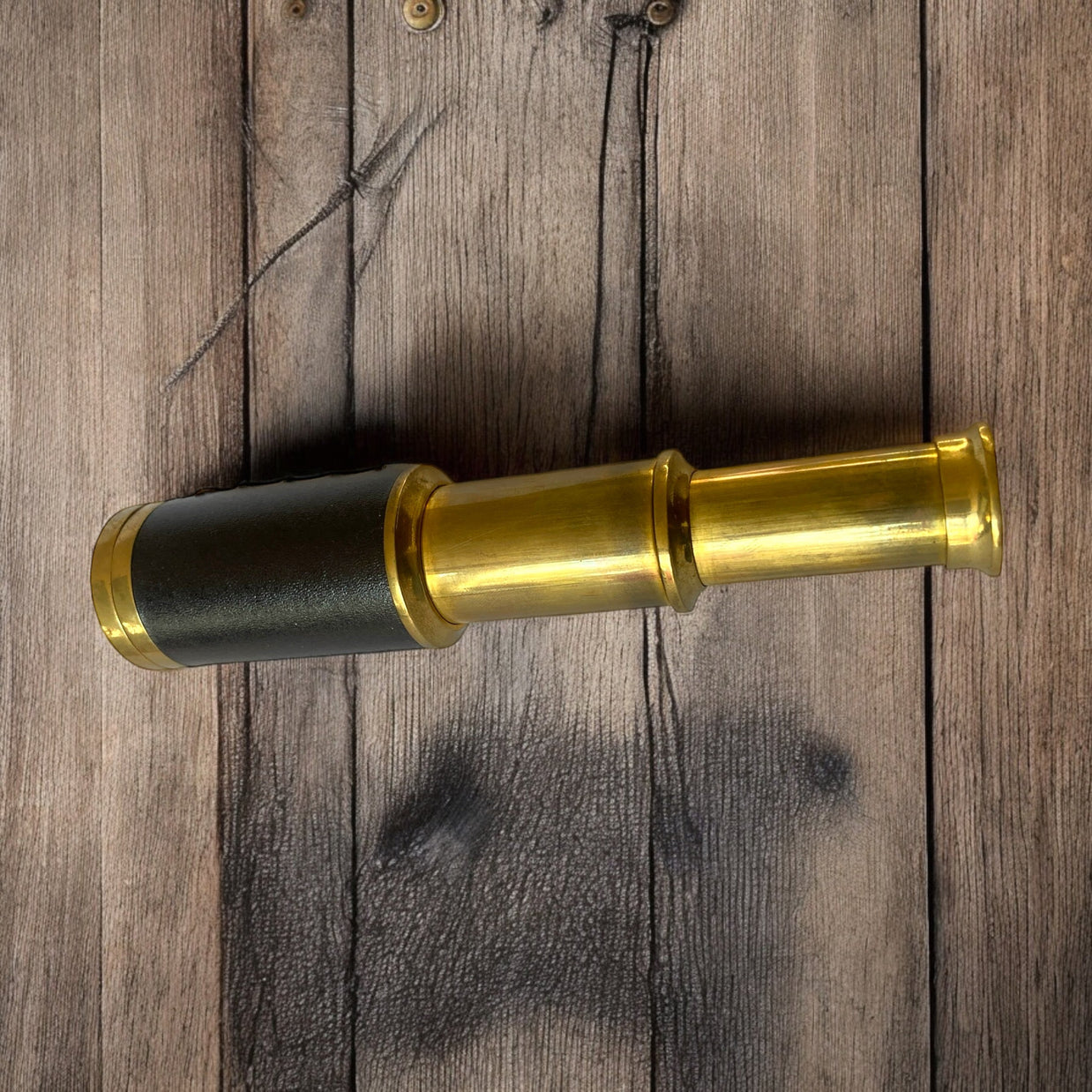 Magis Art Shop vintage style brass monocular telescope with a black leather grip on a rustic wooden background