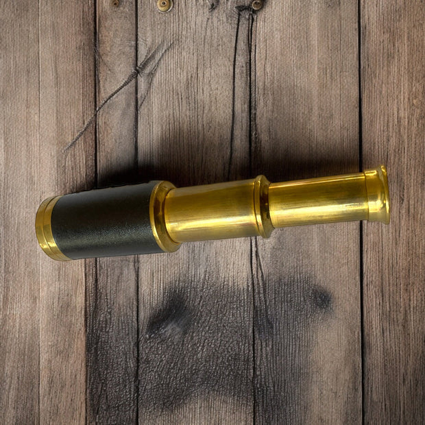 Magis Art Shop vintage style brass monocular telescope with a black leather grip on a rustic wooden background
