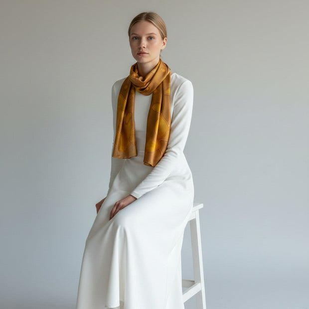 Magis Art Shop hand-painted brown and honey silk scarf worn by a woman in a white dress against a neutral background