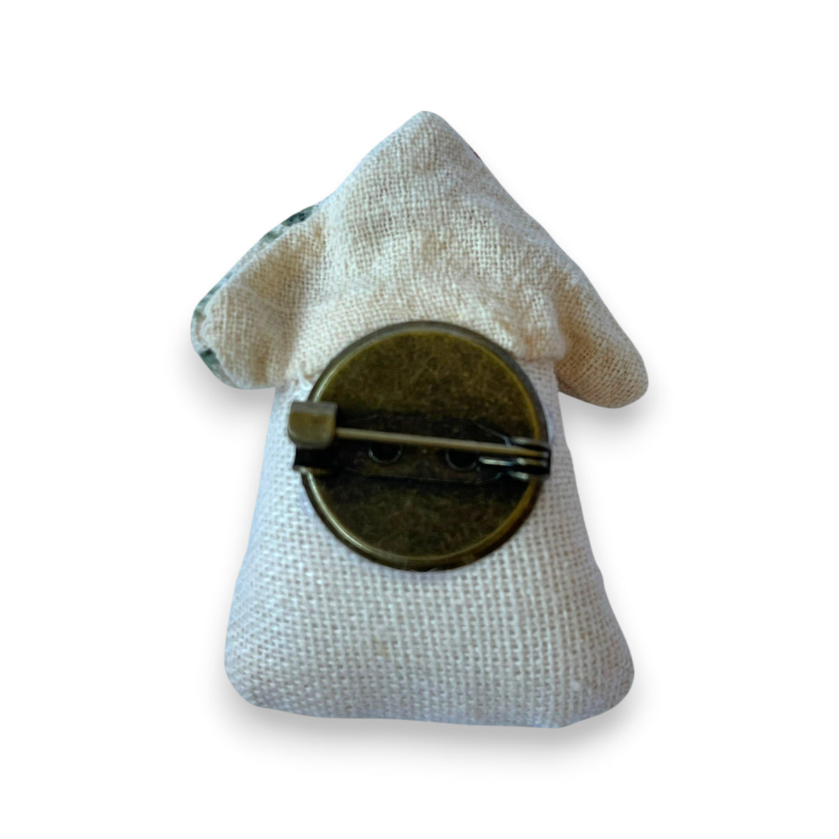 Back view of a Magis Art Shop handmade fabric house brooch with a bronze pin fastener on a cream linen background.