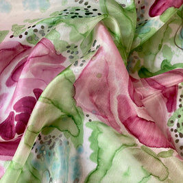 Magis Art Shop silk scarf featuring a vibrant watercolor floral print in shades of pink, green, and soft blue.