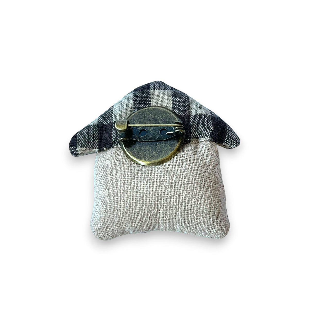 Magis Art Shop small house-shaped textile brooch with a brown and black checkered roof and beige linen base.