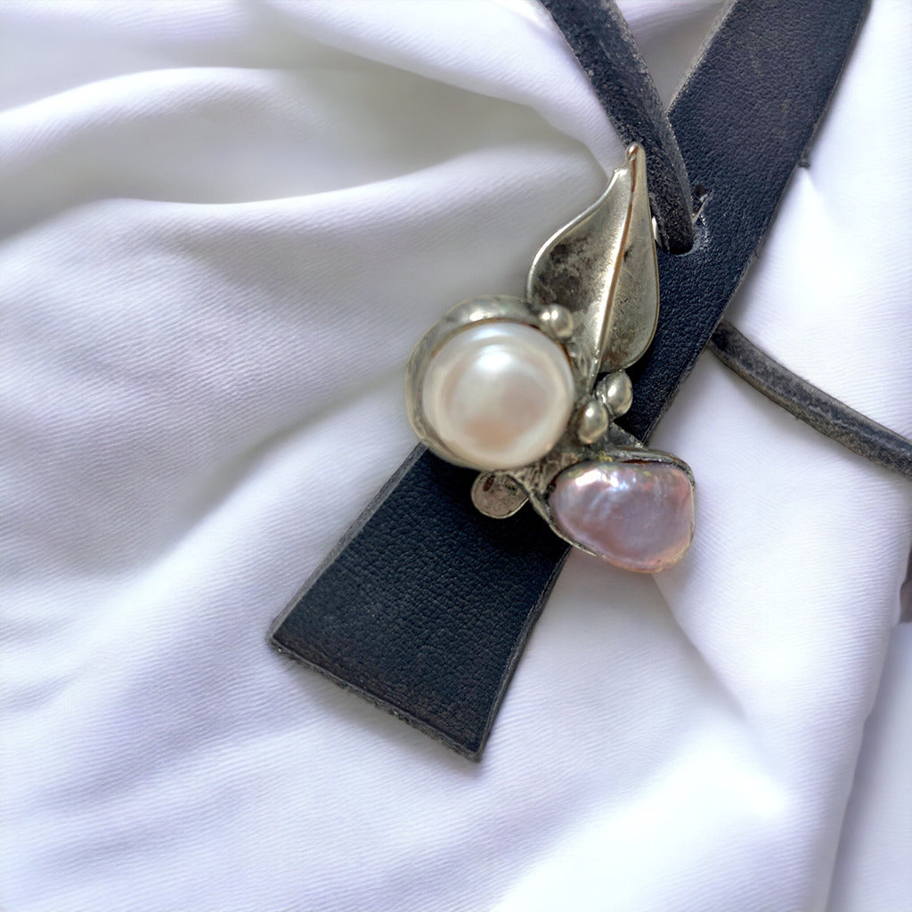 Magis Art Shop leather necklace with a soldered metal leaf pendant and two freshwater pearls on a white fabric