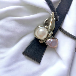 Magis Art Shop leather necklace with a soldered metal leaf pendant and two freshwater pearls on a white fabric