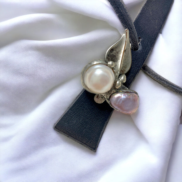 Magis Art Shop leather necklace with a soldered metal leaf pendant and two freshwater pearls on a white fabric