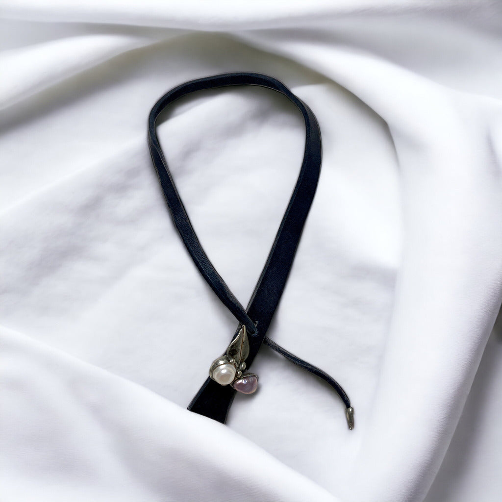 Magis Art Shop leather necklace featuring a tin-soldered leaf pendant with freshwater pearls on a white fabric background