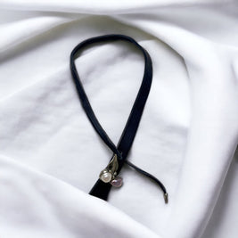 Magis Art Shop leather necklace featuring a tin-soldered leaf pendant with freshwater pearls on a white fabric background