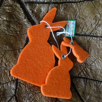 Magis Art Shop orange felt bunny hanging decorations in two different sizes on a dark leaf background