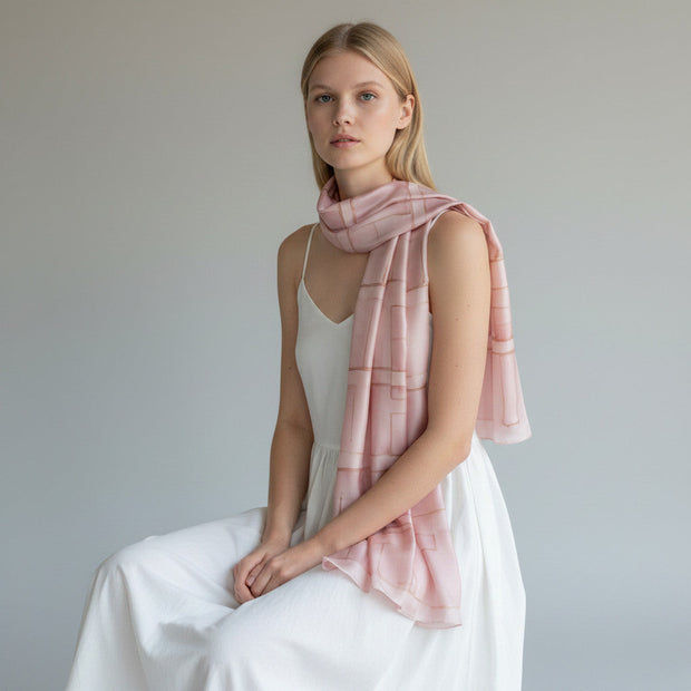 Model wearing a hand-painted light pink silk scarf by Magis Art Shop with a subtle geometric pattern.