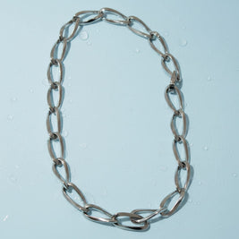 Magis Art Shop stainless steel chain necklace with large oval links and a secure clasp on a light blue background.