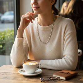 Magis Art Shop minimalist stainless steel link necklace worn by a woman in a cream sweater at a cafe table